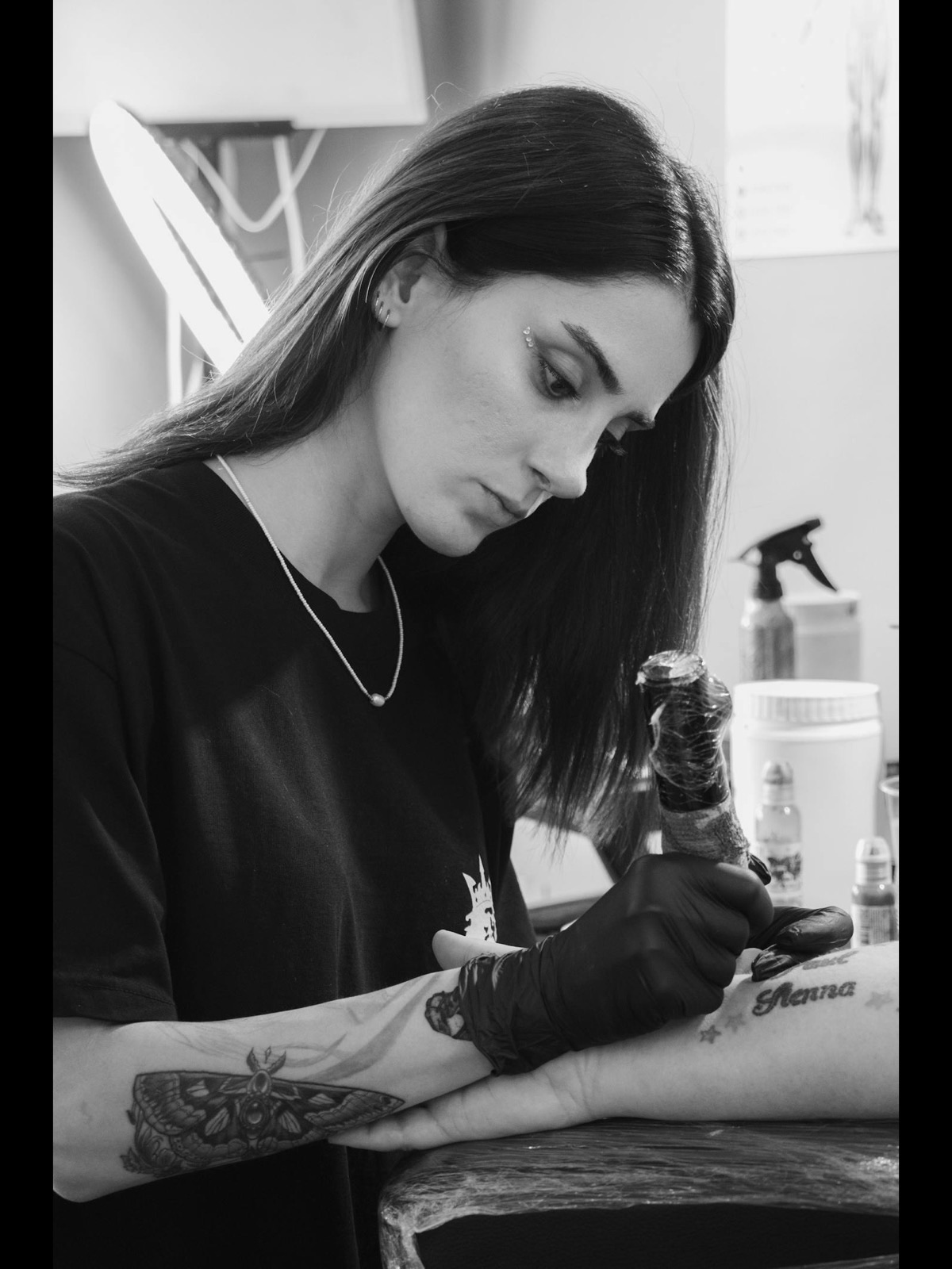 Alissa Jung, owner and head tattoo artist, focused at work in the studio — black gloves and machine in hand, mid-session on a client's forearm.