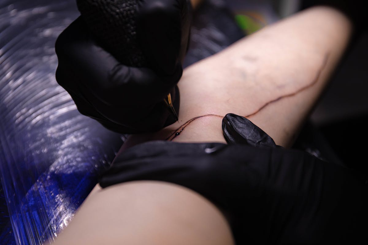 Tattoo session in progress: black-gloved hands and machine working a forearm.
